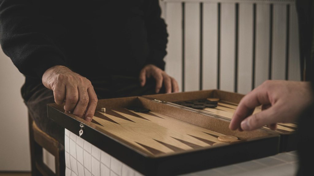 Eine Nahaufnahme von Händen, die drinnen Backgammon spielen, fängt einen Moment der Muße und Strategie ein.